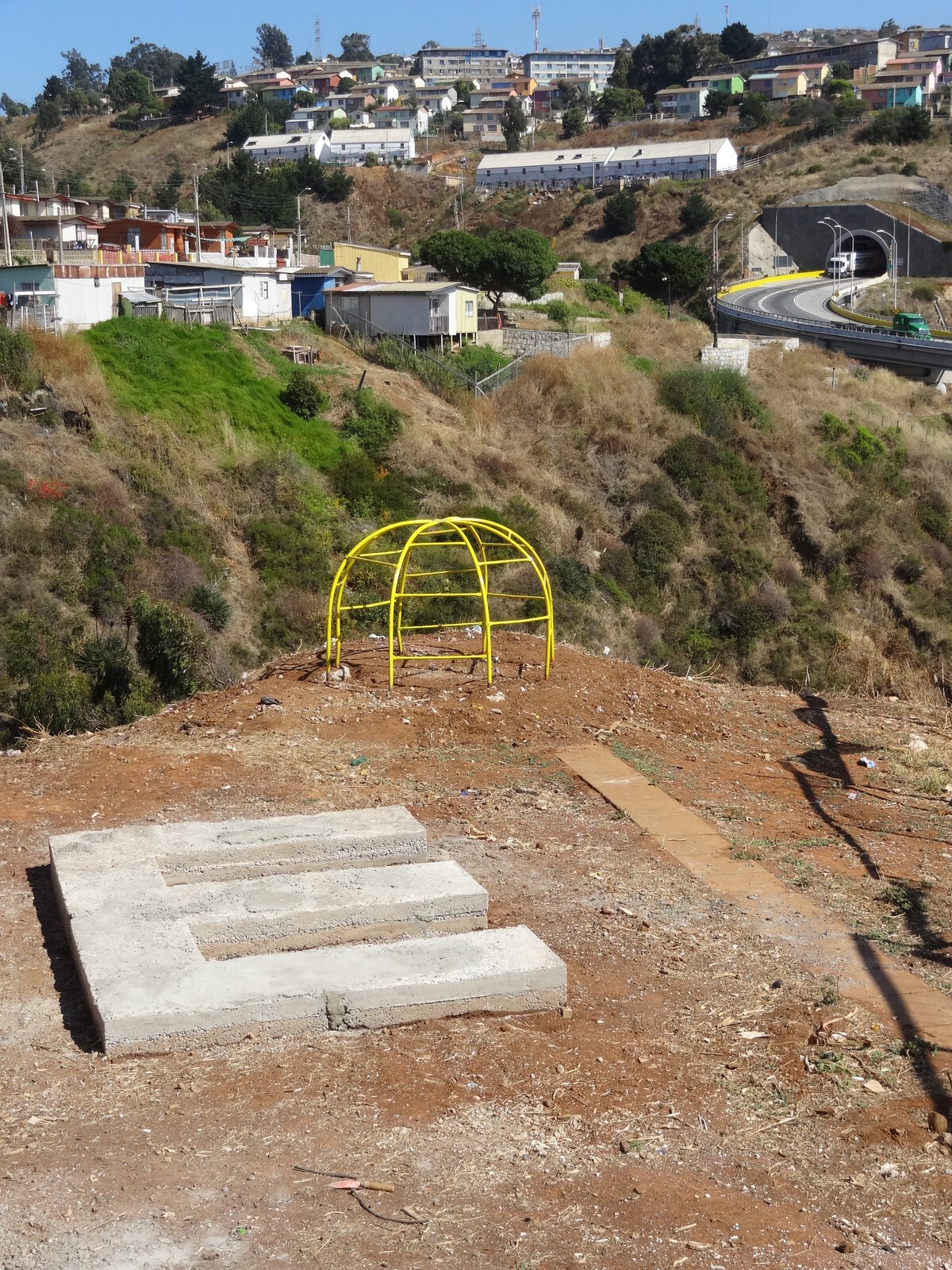 La letra E de El Séptimo Peldaño terminada en concreto, con vista general del cerro, juego infantil amarillo y viaducto, Costa Brava, Playa Ancha