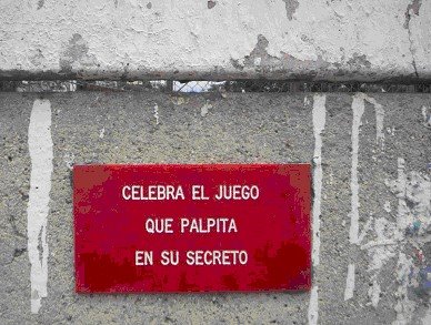 Placa roja con el texto «Celebra el juego que palpita en su secreto» sobre un muro