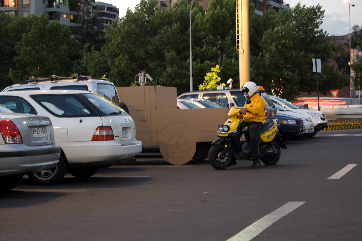 Pieza de Cartón, camioneta LUV en un estacionamiento junto a un guardia en moto