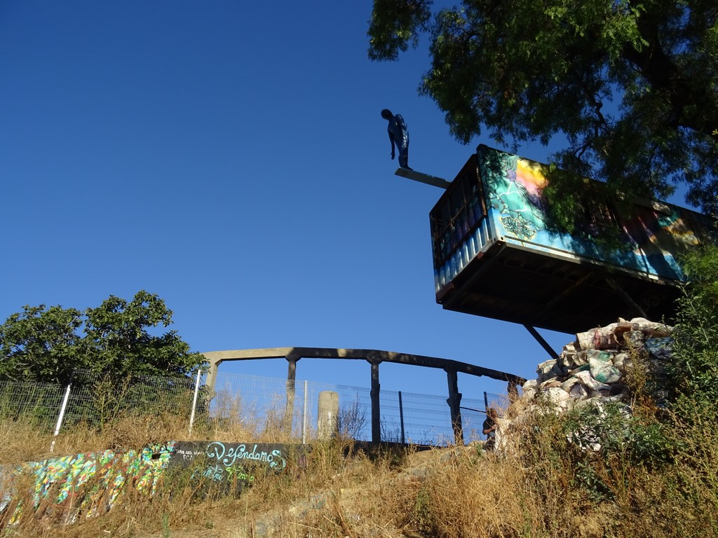 El Nadador Nº 4, el contenedor sobre la quebrada junto a un puente peatonal y el grafiti Defendamos