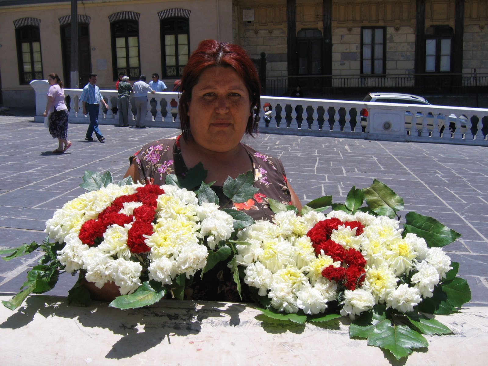 Mujer sosteniendo un arreglo floral con letras rojas y blancas, en una plaza de Valparaíso